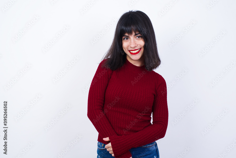 Unhappy Young beautiful Caucasian woman wearing red T-shirt against white wall, crying while posing at camera whipping tears with hand.
