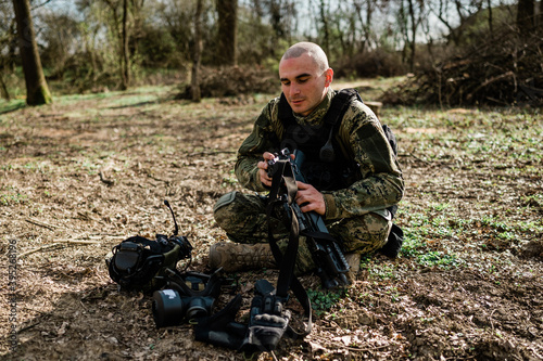 Soldier un Cropat uniform fixing his assault rifle G36 in the forest on a sunny day.