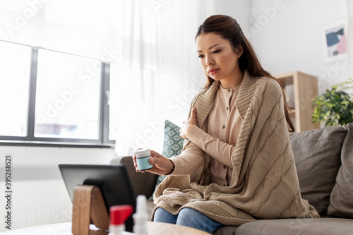 healthcare, technology and people concept - sick asian woman in blanket with medicine having video call on tablet pc computer at home