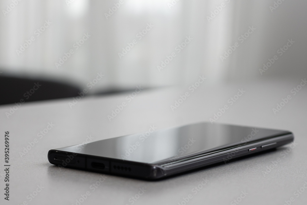Black modern mobile phone with blank screen on black stone table background. Smartphone on old dark grey vintage texture background.