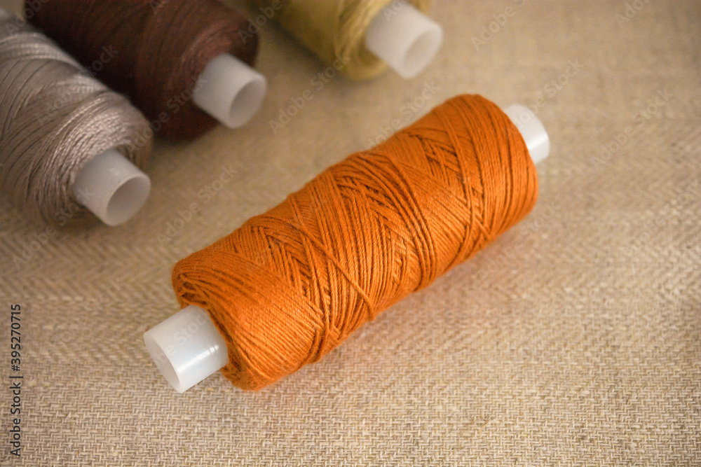 Threads are orange. Sewing accessories lie on a piece of fabric in natural colors. Threads are orange. Sewing accessories lie on a piece of fabric in natural colors.