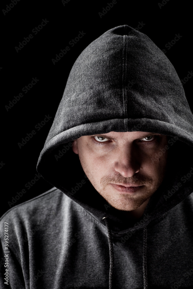 Dark low key portrait of a man looking at camera with a serious facial expression, wearing gray hood Dark low key portrait of a man looking at camera with a serious facial expression, wearing gray hood