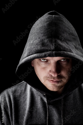 Dark low key portrait of a man looking at camera with a serious facial expression, wearing gray hood