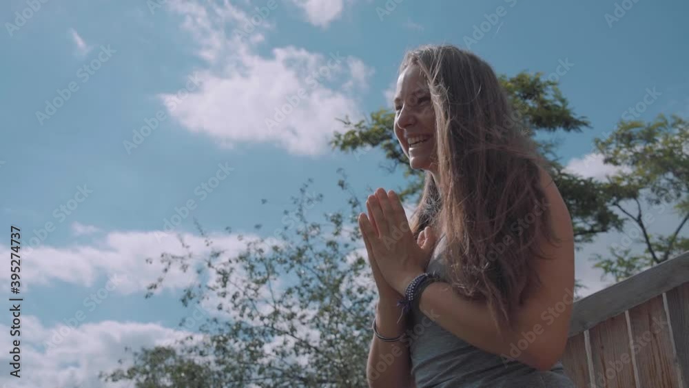 Smiling pretty white woman with hands folded in namaste yoga pose, practicing gratitude in forest. Low angle view. Smiling pretty white woman with hands folded in namaste yoga pose, practicing gratitude in forest. Low angle view.