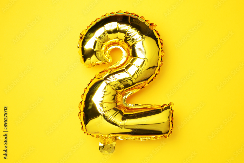 Creative layout. Golden foil balloon number and digit two 2. Birthday greeting card. Anniversary concept. Top view. Copy space. Stylish gold numeral over yellow background. Numerical digit. Creative layout. Golden foil balloon number and digit two 2. Birthday greeting card. Anniversary concept. Top view. Copy space. Stylish gold numeral over yellow background. Numerical digit.