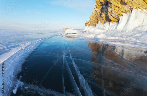 A beautiful winter landscape of frozen Lake Baikal with transparent blue ice with cracks near the rocky island of Edor on Olkhon at sunset. Natural cold background. Winter holidays, ice travel