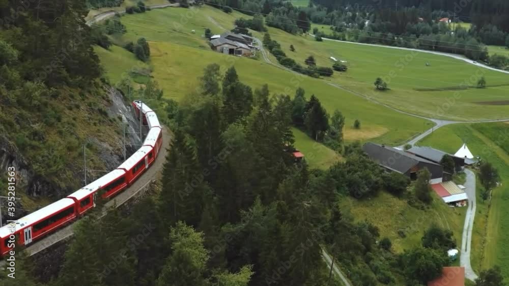 A train running on railway path in Switzerland through mountain and greenery and House