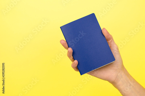 Blue passport without inscriptions in a female hand on a yellow background