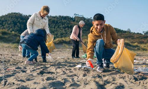 Young man picking up trash with group of volunteers on the beach