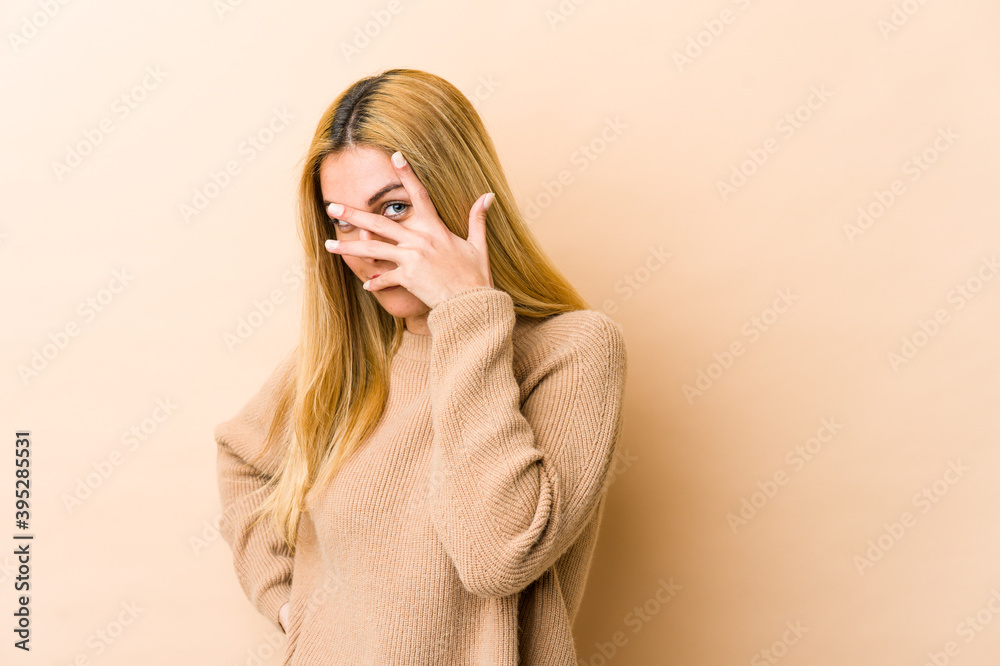 Young blonde caucasian woman blink at the camera through fingers, embarrassed covering face. Young blonde caucasian woman blink at the camera through fingers, embarrassed covering face.