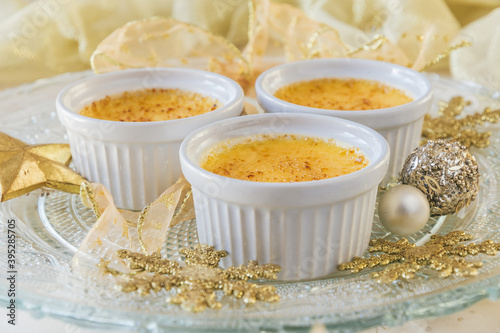 Creme brulee - traditional french vanilla cream dessert with caramelised sugar on top. Three servings served on a decorated glass plate with a golden Christmas decoration.