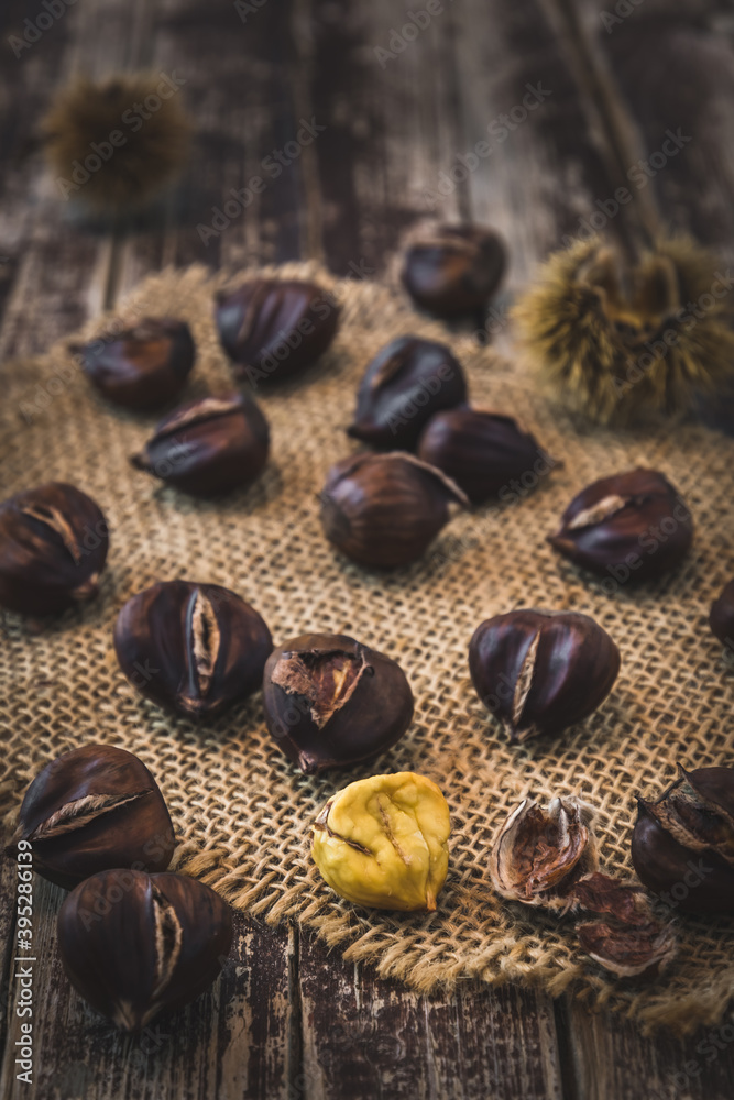 Roasted chestnuts, one peeled, on a dark wooden background, vertical Roasted chestnuts, one peeled, on a dark wooden background, vertical