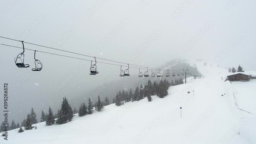 Empty ski lift in snowfall. Chairlifts move under snow storm in mountains ski resort Zell am See Kaprun, Austria. Snowy forest in background. Austrian Alps during bad winter weather, poor visibility Empty ski lift in snowfall. Chairlifts move under snow storm in mountains ski resort Zell am See Kaprun, Austria. Snowy forest in background. Austrian Alps during bad winter weather, poor visibility