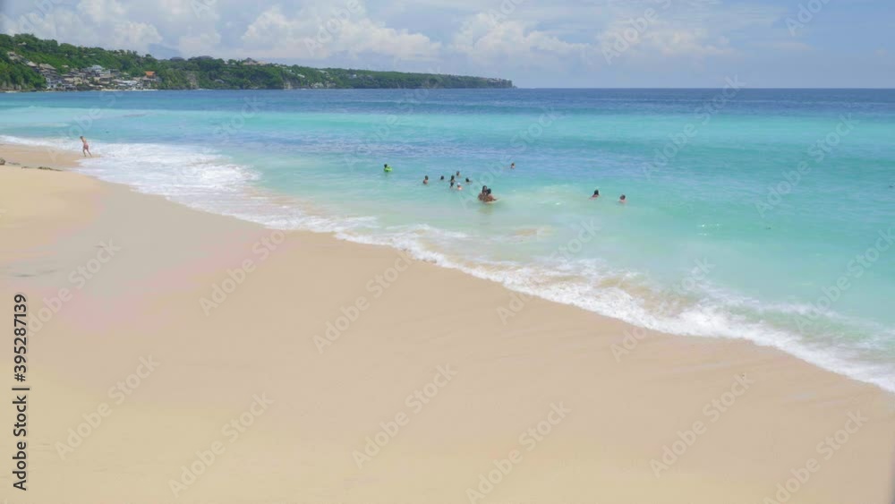 Tourists are swimming, relaxing and having fun in vibrant blue water on tropical beach with big waves in slow motion Tourists are swimming, relaxing and having fun in vibrant blue water on tropical beach with big waves in slow motion