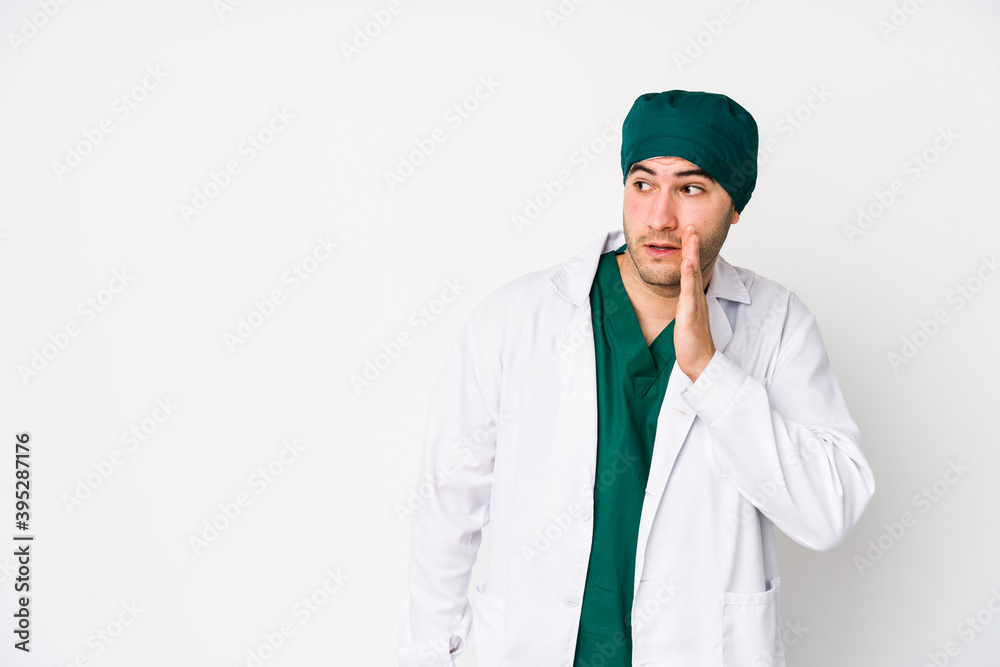 Young surgeon man isolated on white background is saying a secret hot braking news and looking aside Young surgeon man isolated on white background is saying a secret hot braking news and looking aside