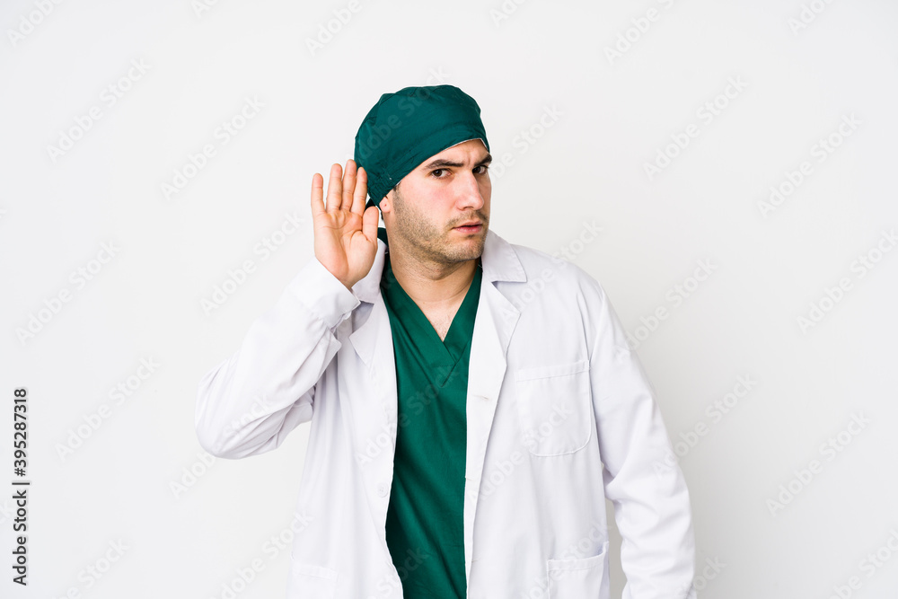 Young surgeon man isolated on white background trying to listening a gossip. Young surgeon man isolated on white background trying to listening a gossip.