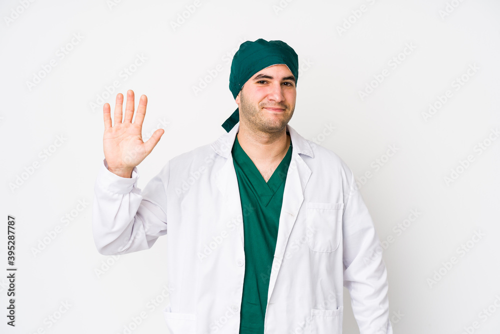 Young surgeon man isolated on white background smiling cheerful showing number five with fingers. Young surgeon man isolated on white background smiling cheerful showing number five with fingers.