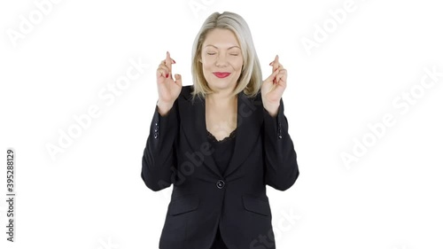 An attractive blonde haired woman is crossing her fingers gesturing for luck and hope. The girl making a wish is wearing a business suit with white background. photo