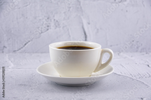 One white cup with aroma refreshing coffee on white plaster background.