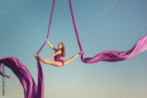 The gymnast artist performs high in the sky. She flies on the canvas showing tricks. photo