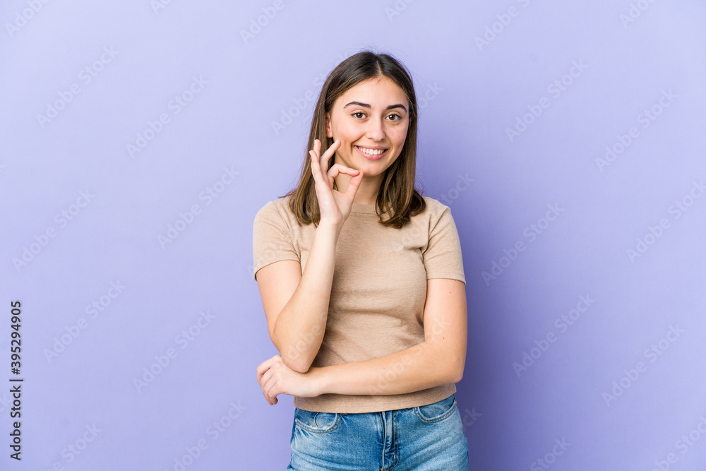 Young caucasian woman winks an eye and holds an okay gesture with hand. Young caucasian woman winks an eye and holds an okay gesture with hand.
