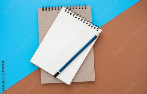 Top view of open school notebook with blank pages with pencil on blue and brown two-tone background. Flat lay, creative workspace office. Business or education concept with copy space.