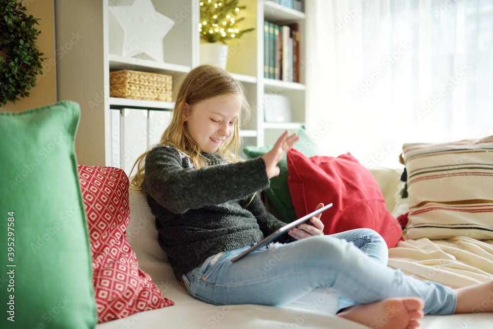 Obraz premium Cute young daughter having online video call on Christmas time. Chatting with distant family during pandemic. Staying safe during winter holidays.