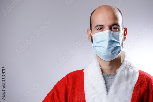 Uomo calvo con mascherina chirurgica e giacca di babbo natale guarda serio, isolato su sfondo bianco photo