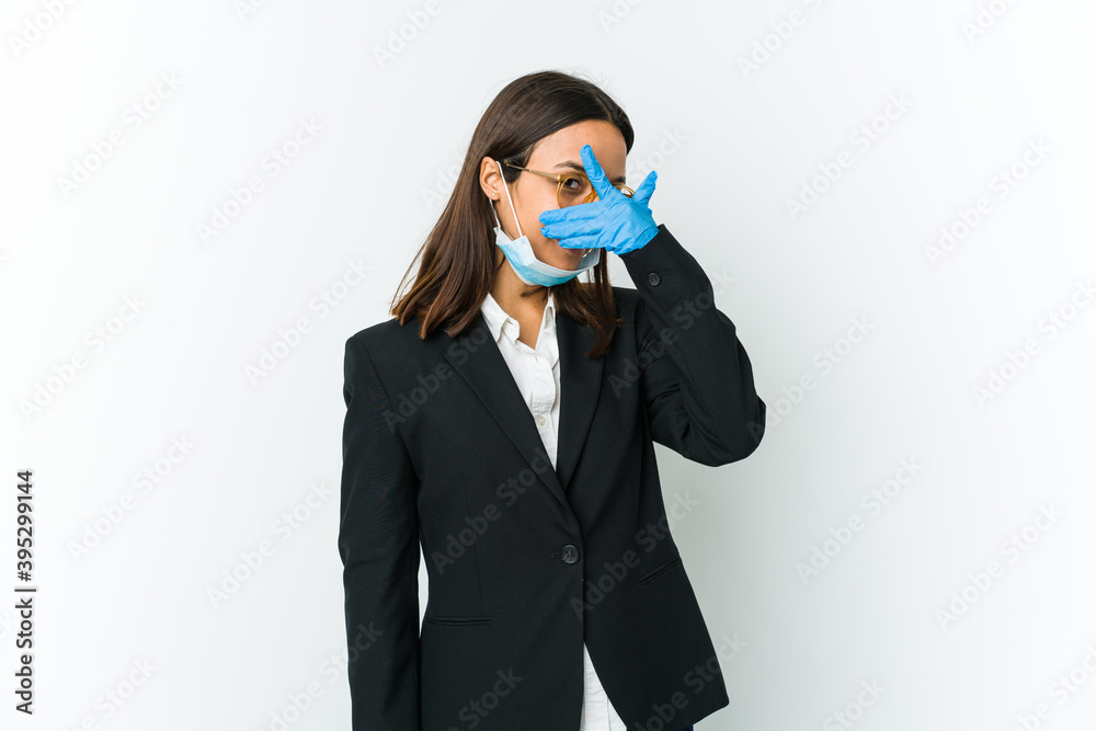 Young business latin woman wearing a mask to protect from covid isolated on white background blink at the camera through fingers, embarrassed covering face. Young business latin woman wearing a mask to protect from covid isolated on white background blink at the camera through fingers, embarrassed covering face.