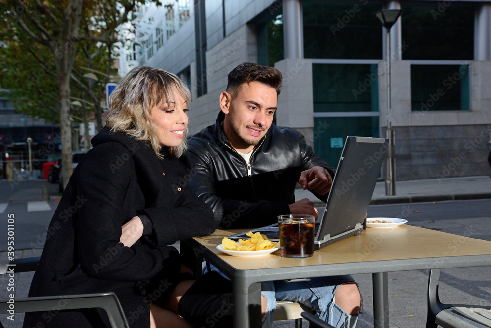 Two young friends having a drink on the terrace of a bar and using a laptop Two young friends having a drink on the terrace of a bar and using a laptop