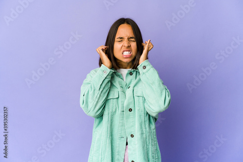 Young mixed race woman covering ears with fingers, stressed and desperate by a loudly ambient.