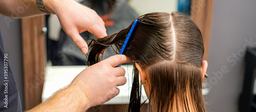 Hands of a hairdresser combing the hair of a young woman parted in sections at the barbershop