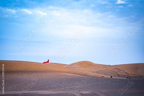 Frau mit rotem Kleid in der Wüste von Abu Dhabi, blauer Himmel und gelber Sand