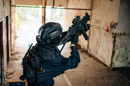 Woman as a police member of swat unit wearing a black jumpsuit and carrying UMP assault rifle. Photos in the abandoned building.
