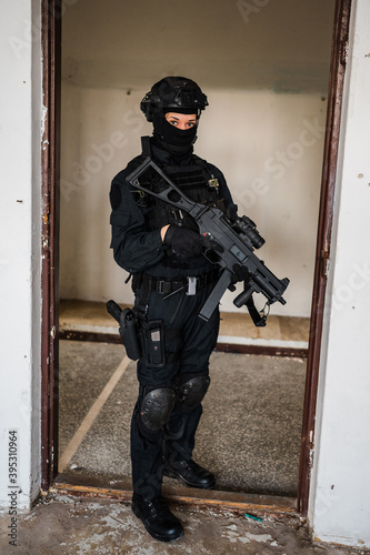 Woman as a police member of swat unit wearing a black jumpsuit and carrying UMP assault rifle. Photos in the abandoned building.