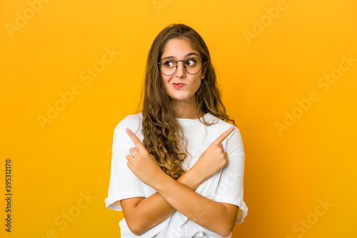 Young caucasian woman points sideways, is trying to choose between two options.