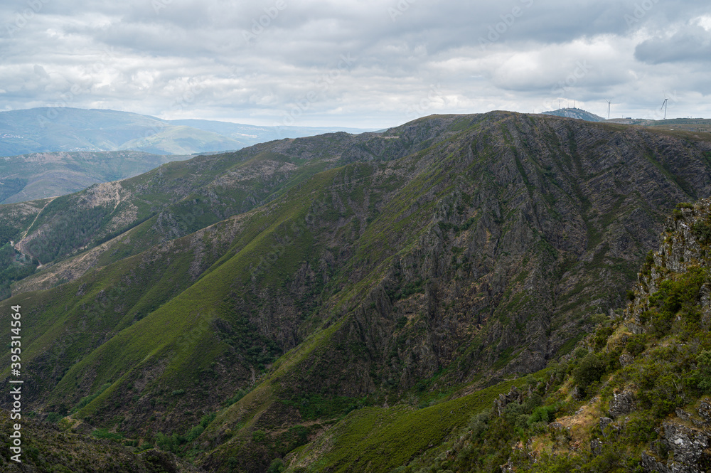 Rugged mountain. Rocky landscape with clouds. Yellow and green vegetation.