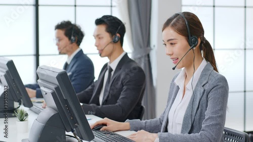 Asian call center team, customer service, telesales in formal suit wearing headset or headphone talking with customer in modern office photo