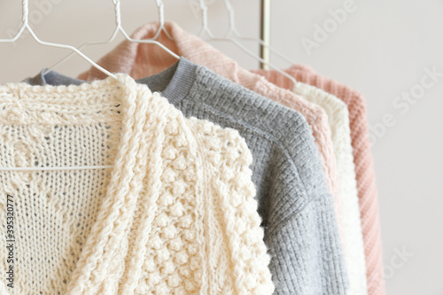 Bunch of knitted warm pastel color sweaters with different vertical knitting patterns hanging on the rack, clearly visible texture. Stylish fall / winter season knitwear clothing. Close up, copy space photo