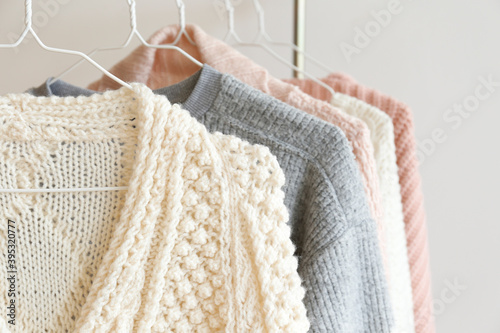 Bunch of knitted warm pastel color sweaters with different vertical knitting patterns hanging on the rack, clearly visible texture. Stylish fall / winter season knitwear clothing. Close up, copy space