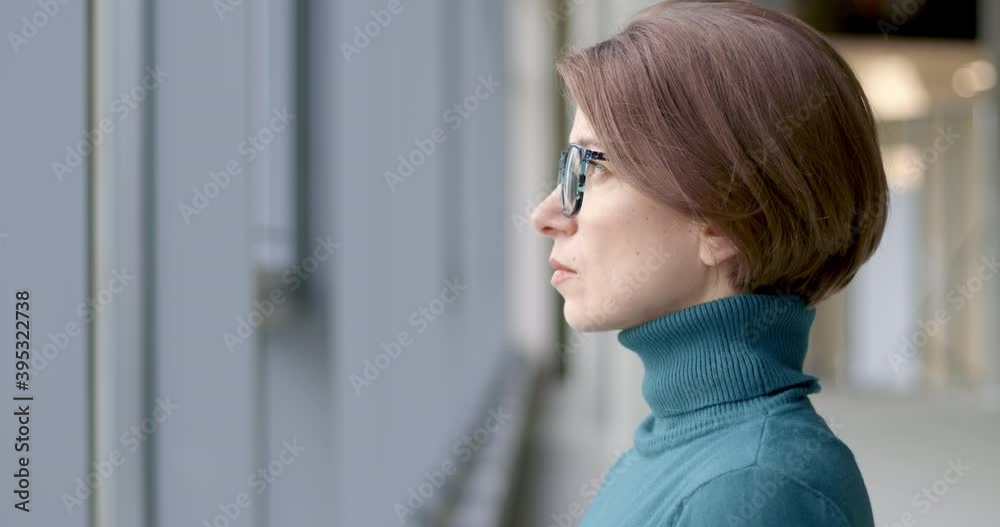 Portrait of a sad young woman with glasses standing by the window. The face of a pensive business woman. Portrait of a sad young woman with glasses standing by the window. The face of a pensive business woman.
