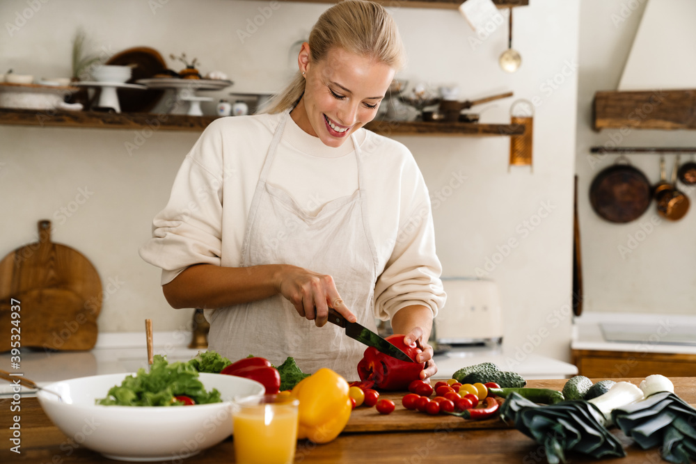 Beautiful happy woman smiling and preparing salad while making lunch Beautiful happy woman smiling and preparing salad while making lunch