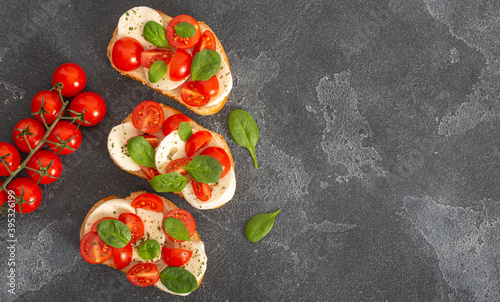 Caprese bruschetta toasts with mozzarella, cherry tomatoes and fresh garden basil.Traditional italian appetizer or snack, antipasto. Top view with copy space. Flat lay.