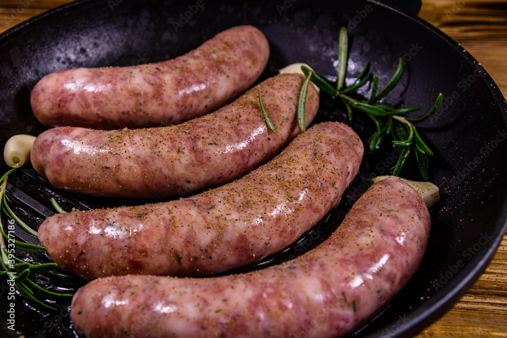 Raw sausages with rosemary twigs and garlic in a cast iron grill pan Raw sausages with rosemary twigs and garlic in a cast iron grill pan