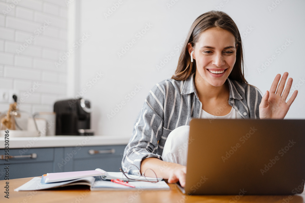 Cheerful beautiful woman waving hand while making online call on laptop Cheerful beautiful woman waving hand while making online call on laptop