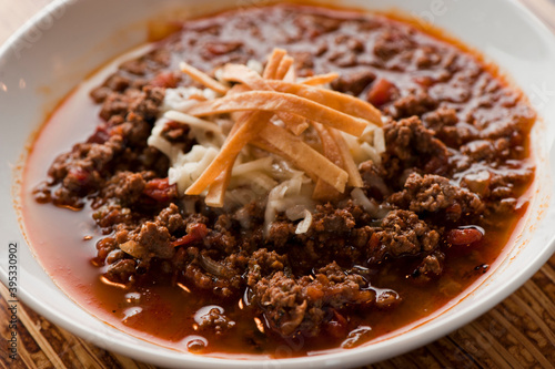 Chili—Texas style five alarm chili. Ground beef seasoned with peppers, spices, onions, slow cooked and served with cheddar cheese and crispy fried tortillas. Traditional southern cooking cuisine.