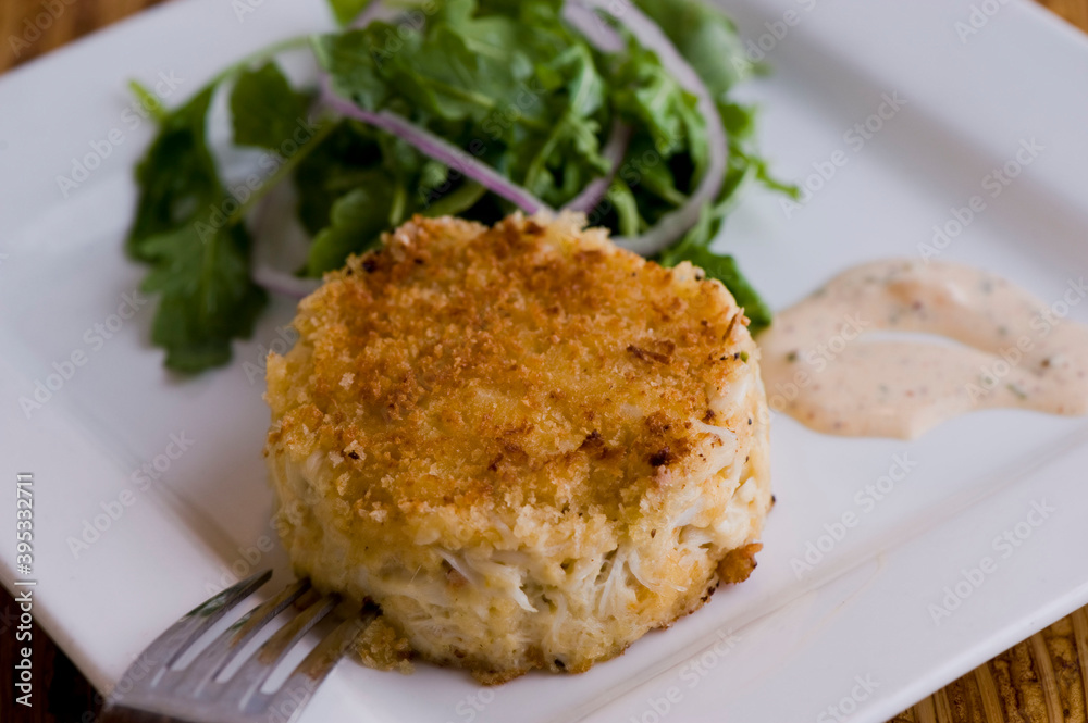 Crab cake. Crab served with spicy rémoulade sauce on top of a mixed green salad. Jumbo crab meat mixed with garlic, onions, spices & fried in butter. Classic American restaurant appetizer.