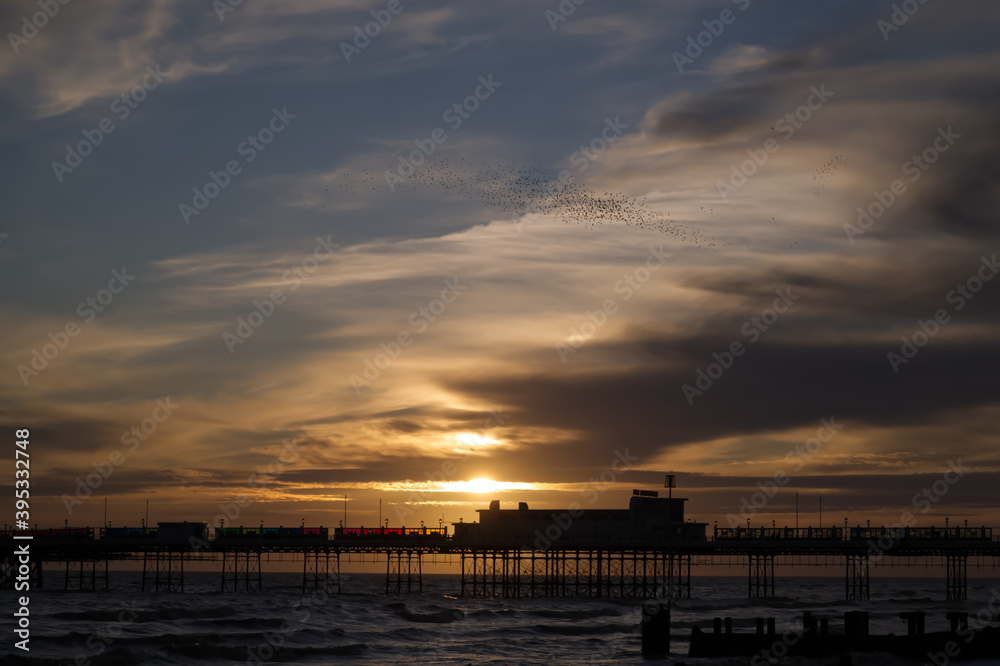Moody beautiful sunset of Worthing Pier with a murmuration of starlings over the pier.