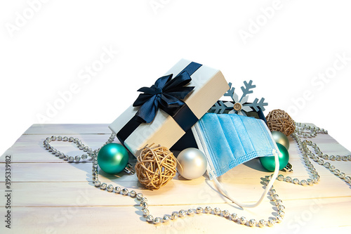 Christmas composition with a gift box, snowflake, disposable mask and Christmas decorations on a white wooden table. The image is isolated on a white background.