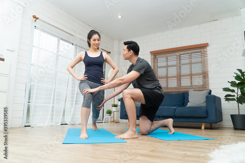 Healthy young Asian couple exercises in home and husband teaching him a wife for exercise in COVID-19 quarantine at home. A new normal lifestyle and healthy exercise can be done anywhere.